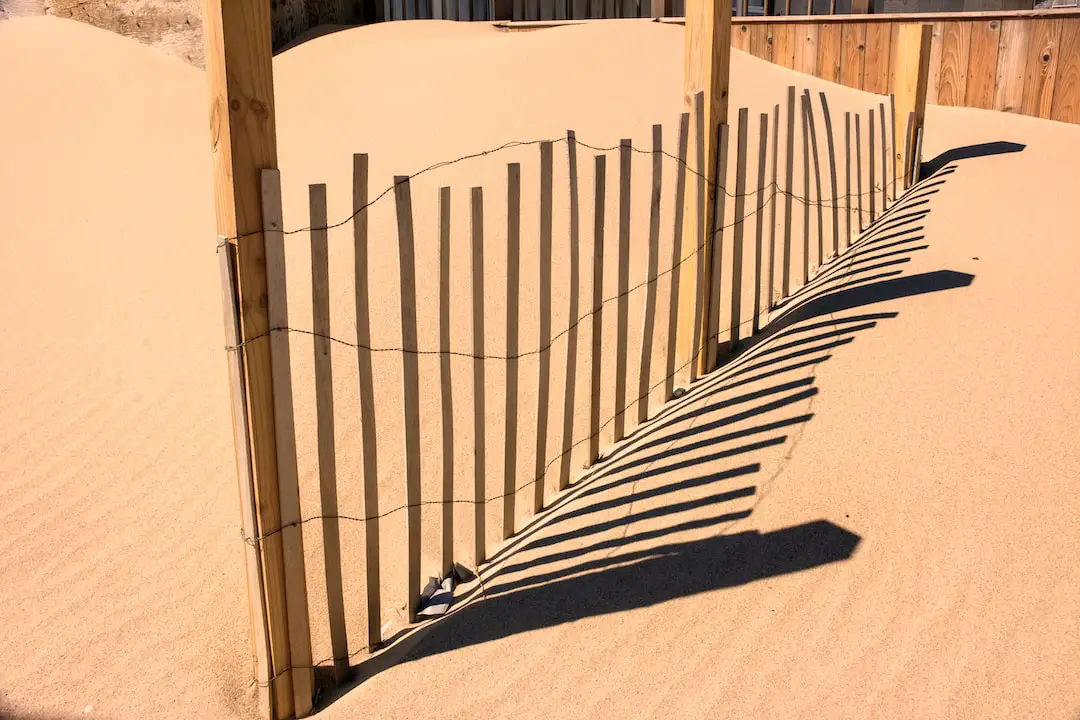 a fence in the sand with a pair of shoes on it