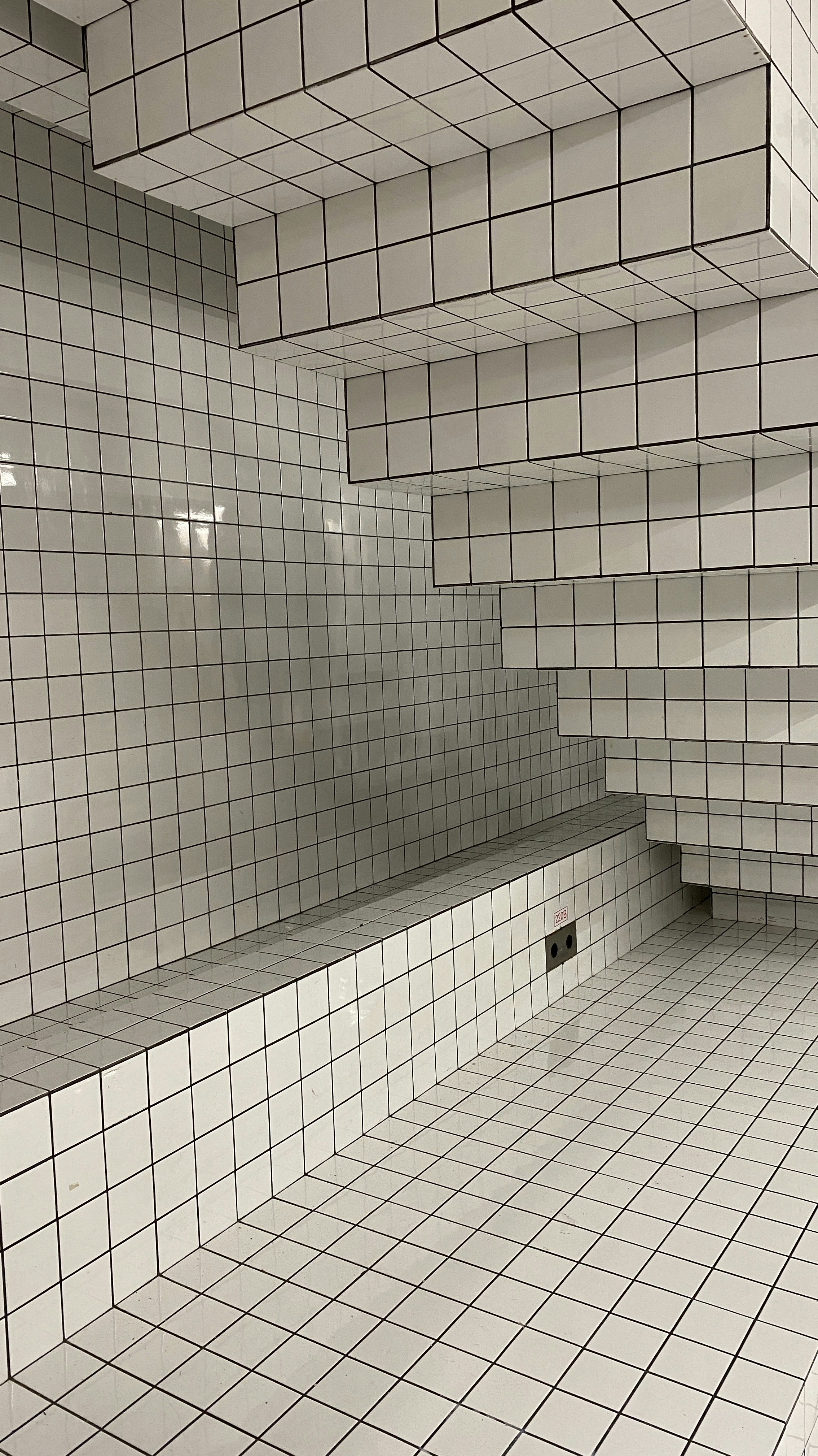 a white tiled room with a bench in the middle